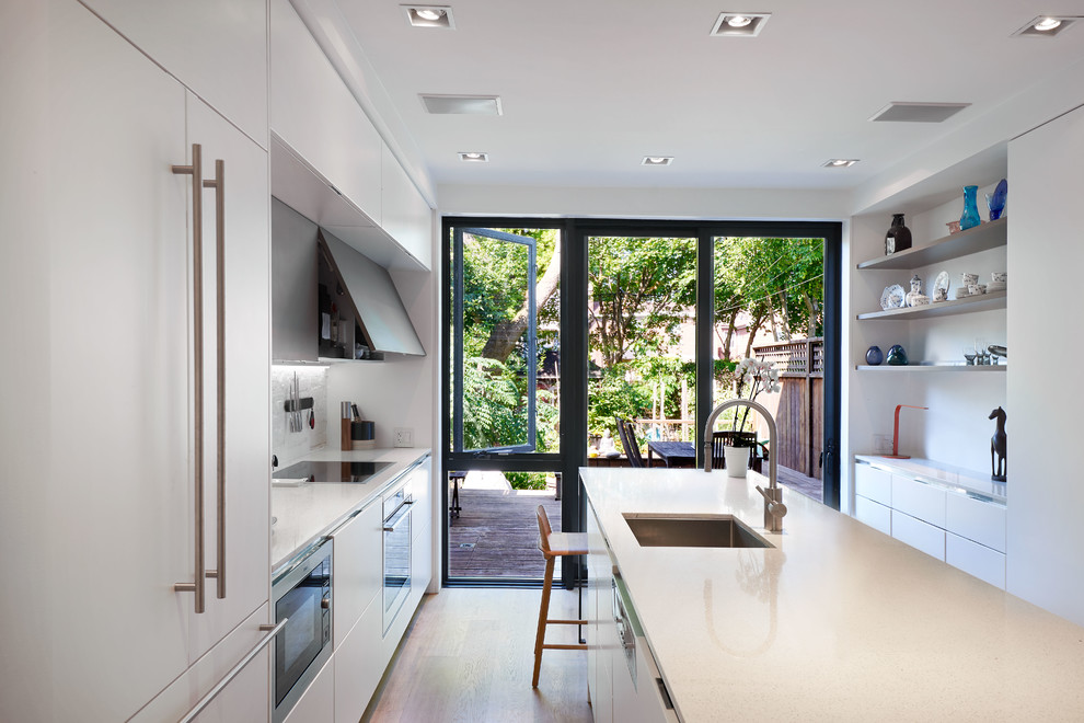 Inspiration for a contemporary kitchen in Toronto with an undermount sink, flat-panel cabinets, white cabinets, white splashback, stainless steel appliances, light hardwood floors and with island.