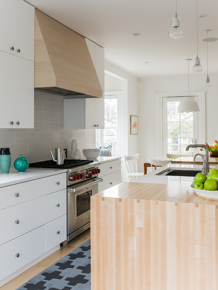 Design ideas for a scandinavian galley eat-in kitchen in Boston with stainless steel appliances, quartz benchtops, a single-bowl sink, flat-panel cabinets, white cabinets, grey splashback, light hardwood floors, with island and ceramic splashback.