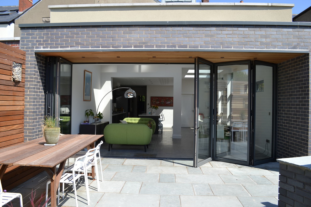 Mid-sized modern backyard patio in Dublin with a roof extension and natural stone pavers.