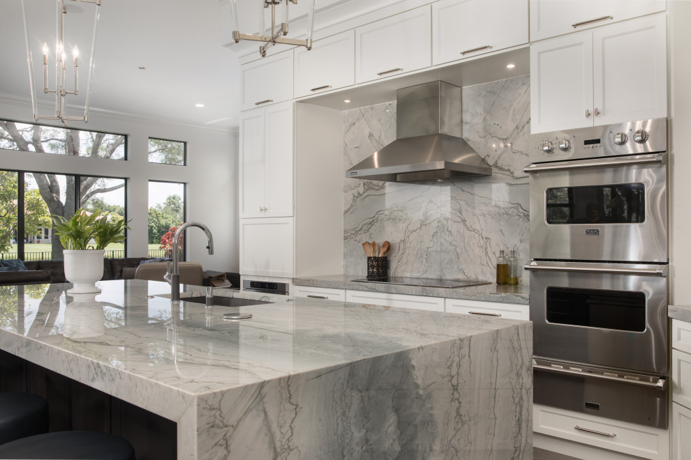 Large transitional l-shaped kitchen photo in Miami with an undermount sink, shaker cabinets, white cabinets, quartzite countertops, gray backsplash, stone slab backsplash, stainless steel appliances, an island and gray countertops