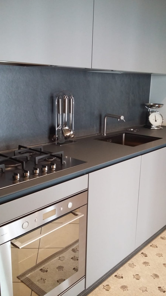 This is an example of a mid-sized modern l-shaped separate kitchen in Turin with an undermount sink, flat-panel cabinets, grey cabinets, laminate benchtops, grey splashback, ceramic splashback, stainless steel appliances, porcelain floors, beige floor and grey benchtop.