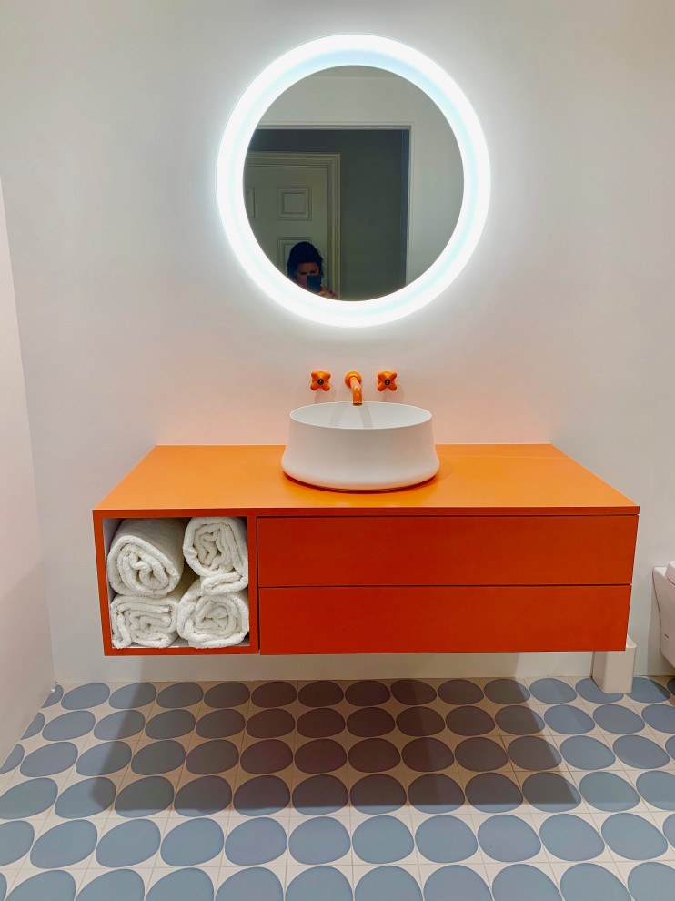 Photo of a mid-sized modern bathroom in Los Angeles with flat-panel cabinets, orange cabinets, a curbless shower, a wall-mount toilet, porcelain tile, white walls, porcelain floors, a vessel sink, laminate benchtops, blue floor, a hinged shower door, orange benchtops and gray tile.