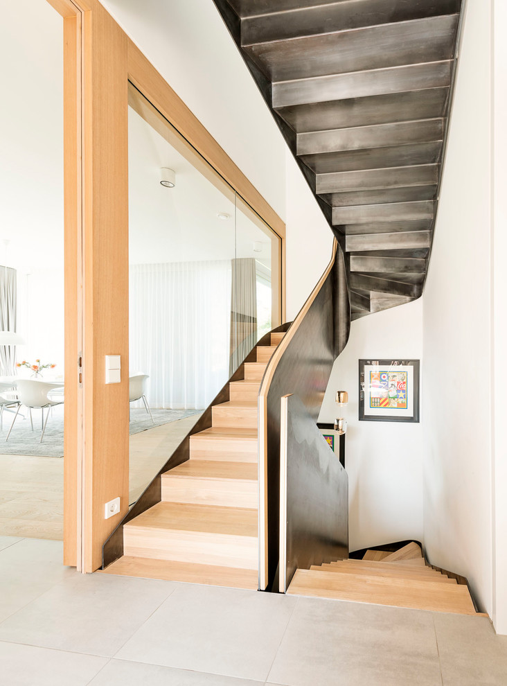 This is an example of a large contemporary wood u-shaped staircase in Munich with wood risers and metal railing.