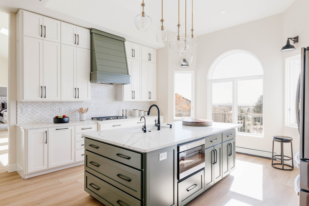 Inspiration for a classic galley kitchen in Denver with a submerged sink, shaker cabinets, white cabinets, white splashback, stainless steel appliances, light hardwood flooring, an island, beige floors and white worktops.