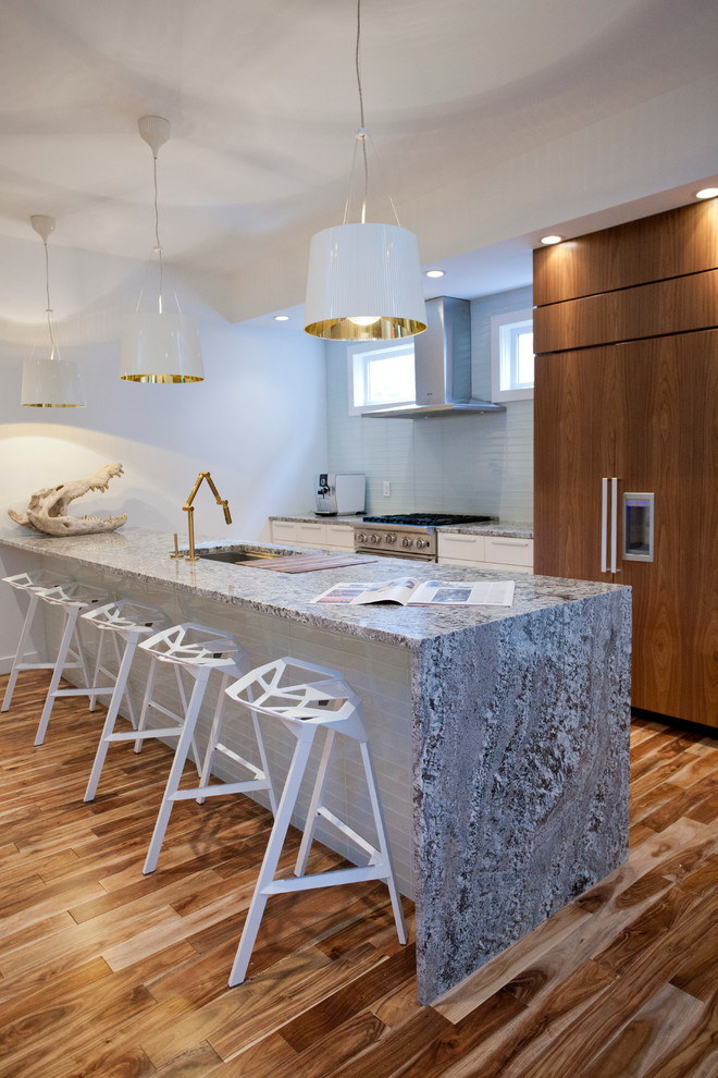 This is an example of a mid-sized contemporary single-wall kitchen in Calgary with an undermount sink, flat-panel cabinets, white cabinets, panelled appliances, medium hardwood floors, with island, white splashback and glass tile splashback.