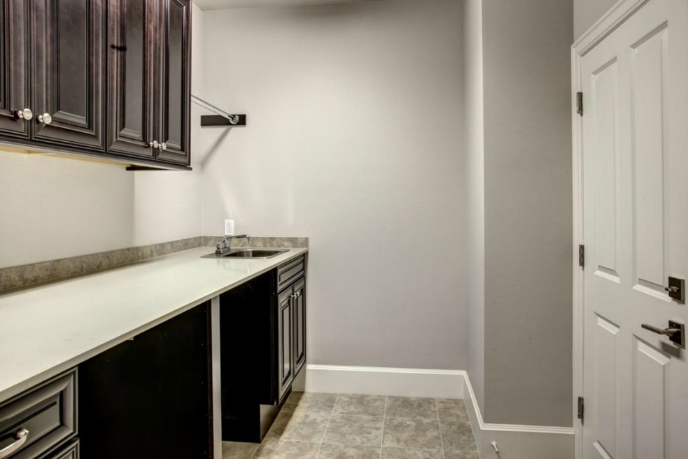 Mid-sized traditional single-wall dedicated laundry room in Seattle with a drop-in sink, recessed-panel cabinets, dark wood cabinets, solid surface benchtops, beige walls, porcelain floors, a side-by-side washer and dryer and multi-coloured floor.