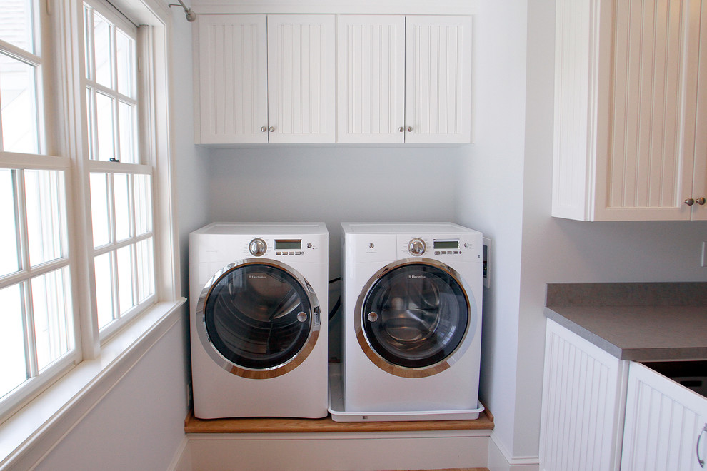 Inspiration for a mid-sized beach style single-wall dedicated laundry room in Portland Maine with white cabinets, solid surface benchtops, white walls, light hardwood floors, a side-by-side washer and dryer, beige floor and recessed-panel cabinets.