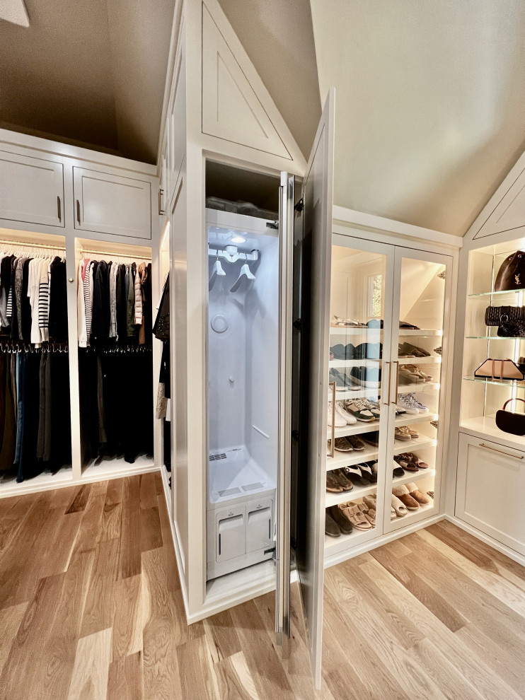 Modelo de armario vestidor unisex y abovedado grande con puertas de armario blancas, suelo de madera clara y suelo beige