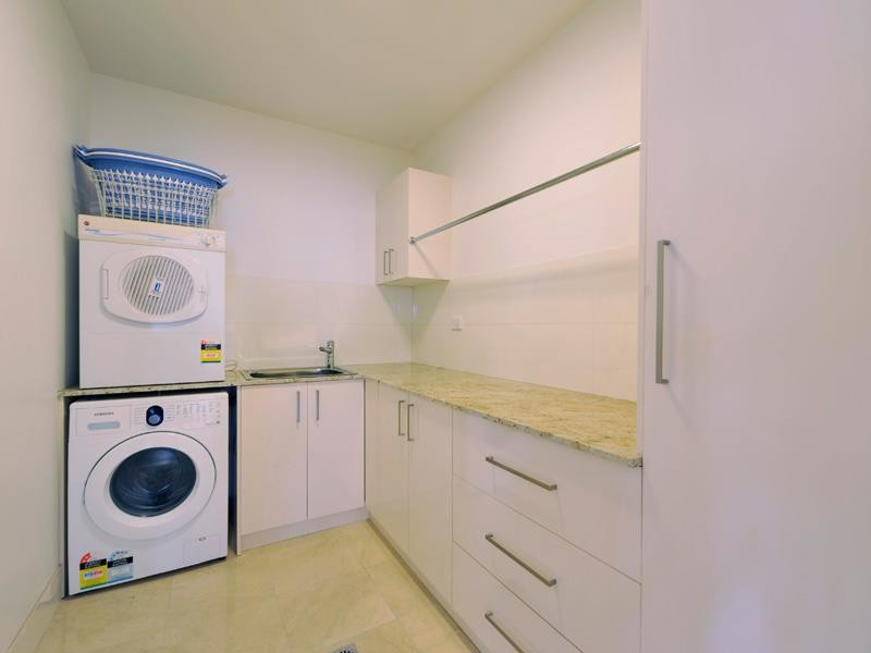 Design ideas for a mid-sized contemporary l-shaped dedicated laundry room in Brisbane with a drop-in sink, flat-panel cabinets, white cabinets, granite benchtops, white walls, marble floors and a stacked washer and dryer.