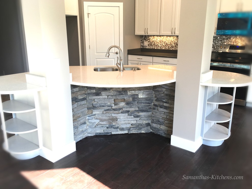Example of a mid-sized transitional l-shaped dark wood floor home design design with an undermount sink, recessed-panel cabinets, white cabinets, quartz countertops, gray backsplash, ceramic backsplash, stainless steel appliances and an island