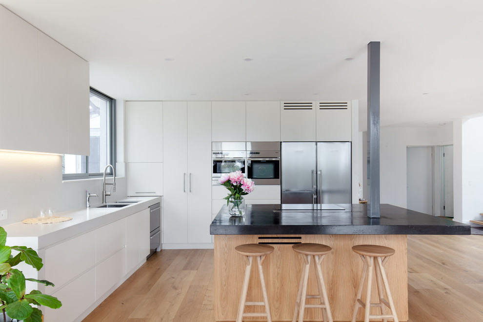 Contemporary l-shaped kitchen in Sydney with an undermount sink, flat-panel cabinets, white cabinets, stainless steel appliances, medium hardwood floors, with island, brown floor and white benchtop.