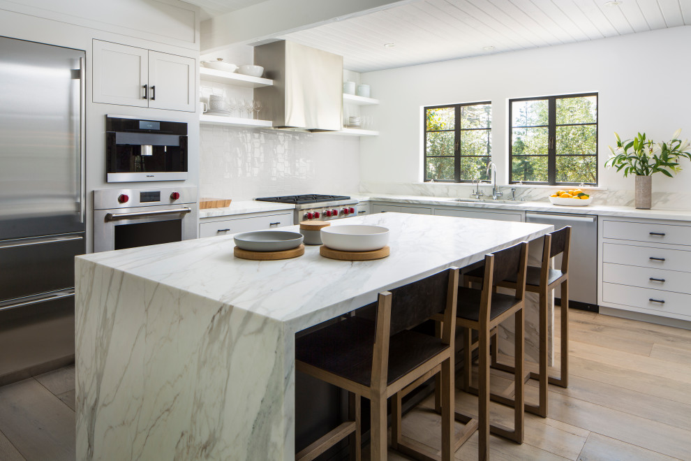 Large transitional l-shaped light wood floor, beige floor and shiplap ceiling kitchen photo in Santa Barbara with white cabinets, stainless steel appliances, an island, white countertops, an undermount sink, flat-panel cabinets and white backsplash