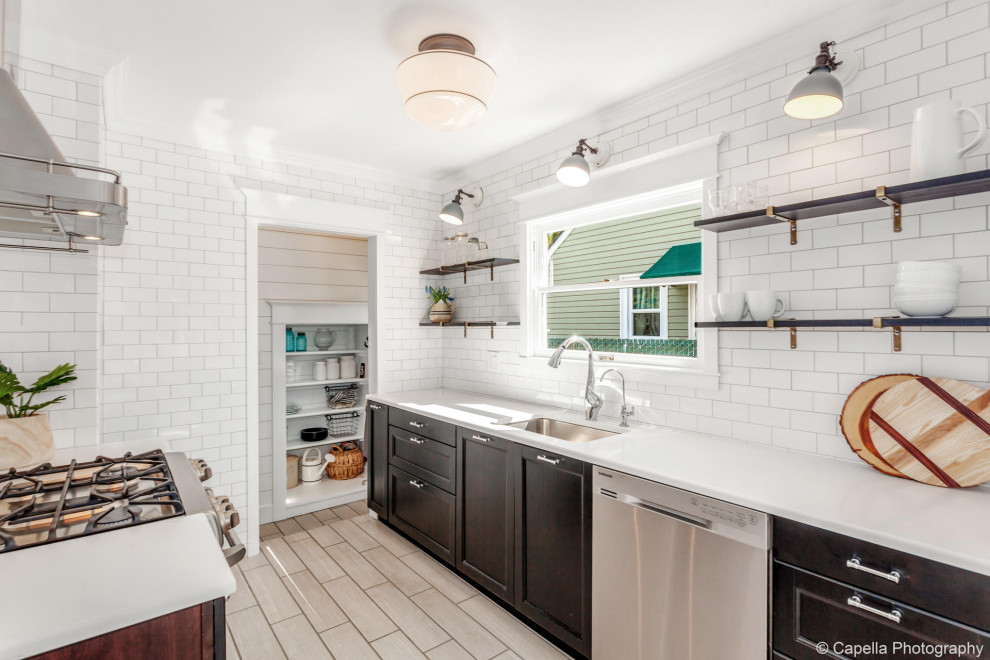 This is an example of a mid-sized arts and crafts galley separate kitchen in Portland with a drop-in sink, recessed-panel cabinets, black cabinets, granite benchtops, white splashback, ceramic splashback, stainless steel appliances, ceramic floors, no island, grey floor and white benchtop.