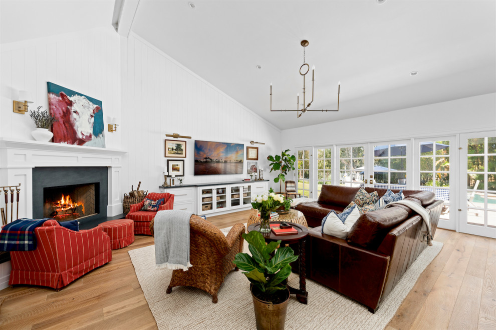 This is an example of a transitional open concept living room in San Diego with white walls, medium hardwood floors, a corner fireplace, brown floor and vaulted.