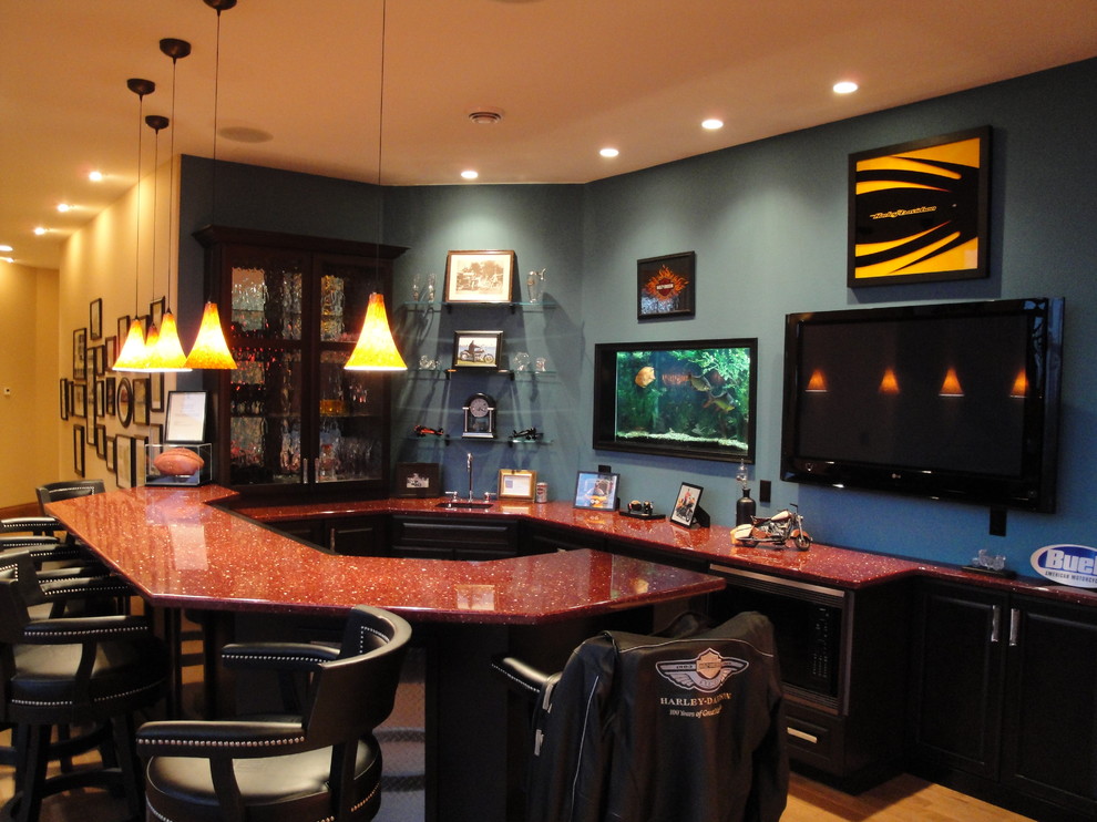 This is an example of an eclectic u-shaped home bar in Milwaukee with black cabinets, quartz benchtops, light hardwood floors and red benchtop.