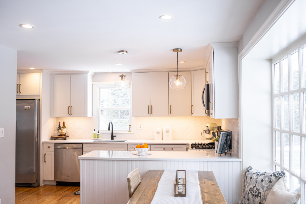 This is an example of a mid-sized transitional l-shaped eat-in kitchen in Baltimore with an undermount sink, shaker cabinets, white cabinets, quartz benchtops, white splashback, cement tile splashback, stainless steel appliances, medium hardwood floors, a peninsula, brown floor and white benchtop.