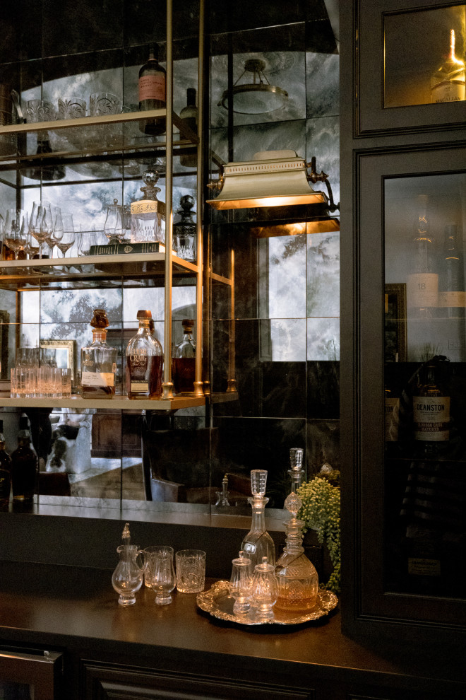 Foto di un angolo bar con lavandino vittoriano di medie dimensioni con ante di vetro, ante nere, top in saponaria, paraspruzzi a specchio, pavimento in legno massello medio, pavimento marrone e top nero