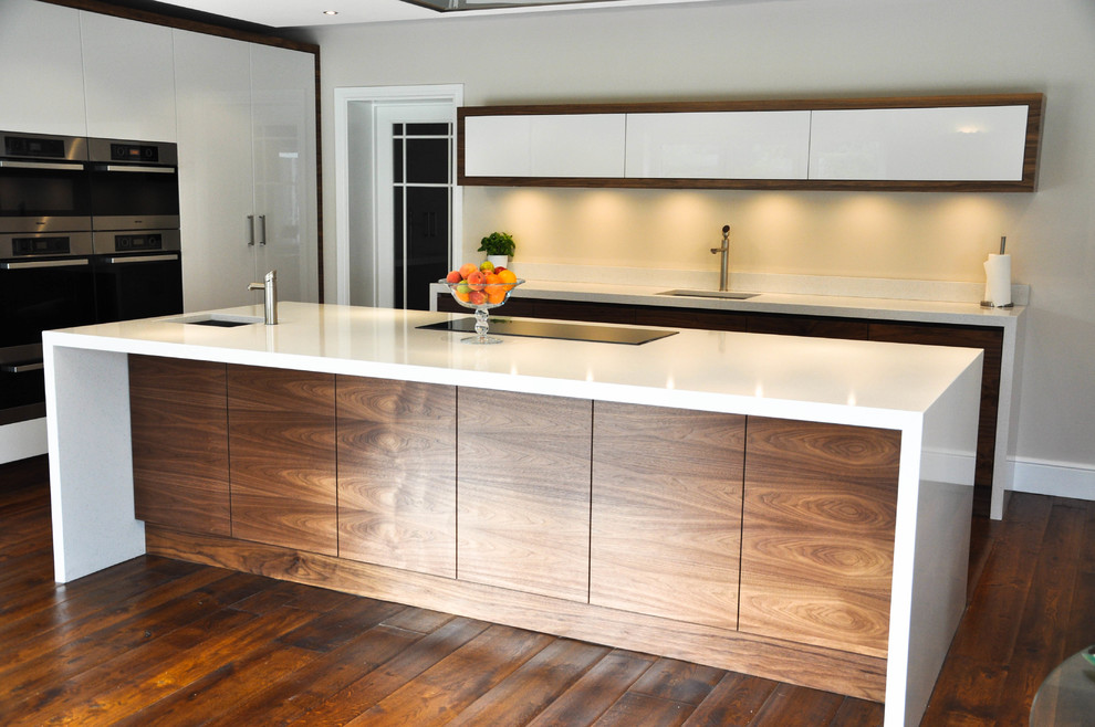 This is an example of a large contemporary l-shaped open plan kitchen in Surrey with a drop-in sink, flat-panel cabinets, dark wood cabinets, quartzite benchtops, stainless steel appliances, dark hardwood floors and with island.