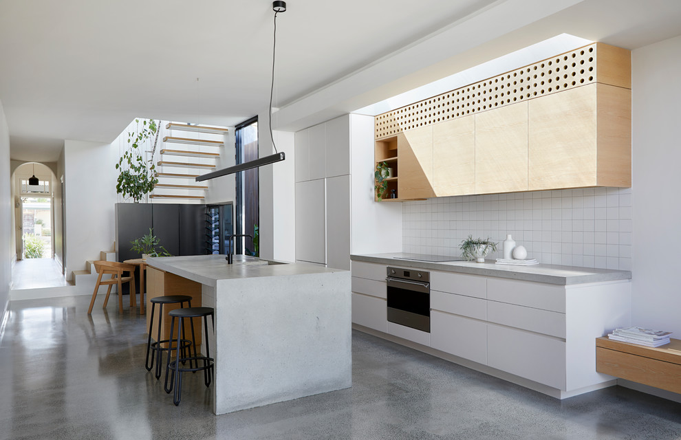 Inspiration for a mid-sized contemporary galley open plan kitchen in Melbourne with light wood cabinets, concrete benchtops, white splashback, ceramic splashback, stainless steel appliances, concrete floors, with island, grey floor, grey benchtop, an integrated sink and flat-panel cabinets.