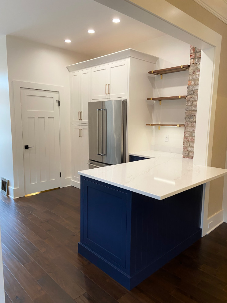 Mid-sized traditional u-shaped eat-in kitchen in Seattle with a farmhouse sink, recessed-panel cabinets, blue cabinets, quartz benchtops, white splashback, ceramic splashback, stainless steel appliances, medium hardwood floors, a peninsula, brown floor and white benchtop.