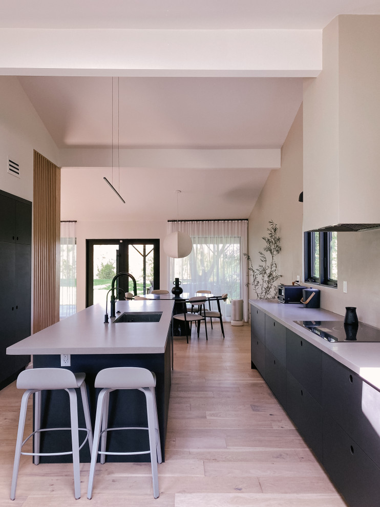Modern inredning av ett stort grå linjärt grått kök och matrum, med en rustik diskho, släta luckor, svarta skåp, granitbänkskiva, grått stänkskydd, stänkskydd i cementkakel, svarta vitvaror, ljust trägolv, en köksö och beiget golv