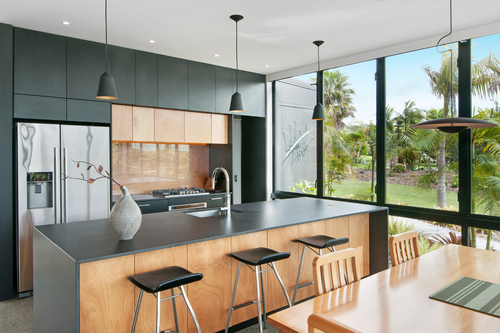 This is an example of a contemporary galley eat-in kitchen in Auckland with an undermount sink, flat-panel cabinets, light wood cabinets, beige splashback, glass sheet splashback, stainless steel appliances and with island.