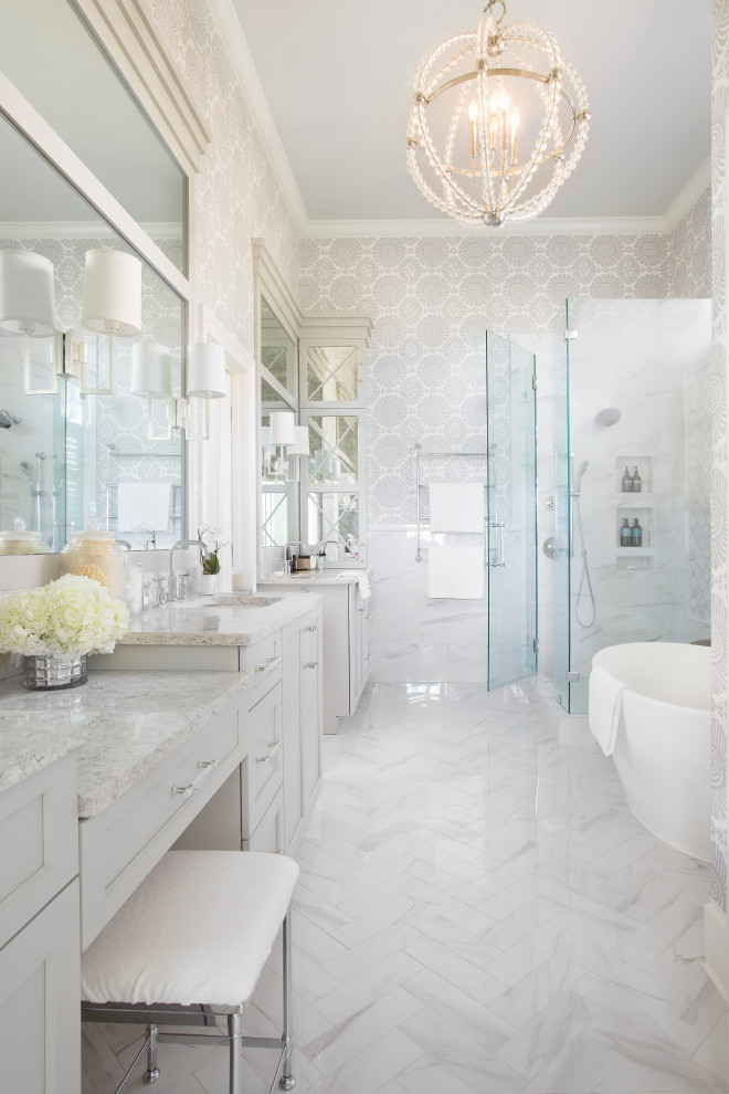 This is an example of a mid-sized traditional master bathroom in Charleston with recessed-panel cabinets, grey cabinets, white tile, porcelain tile, porcelain floors, an undermount sink, engineered quartz benchtops, white floor, a hinged shower door, grey benchtops, an enclosed toilet, a double vanity, a built-in vanity, wallpaper and a freestanding tub.