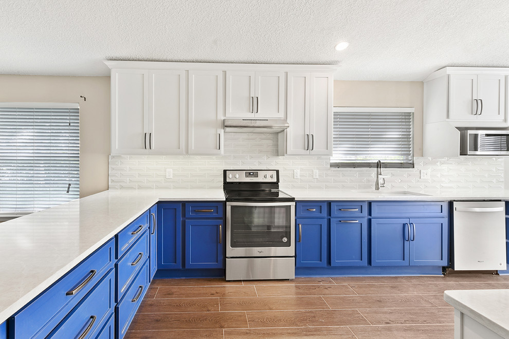 Open concept kitchen - large transitional l-shaped vinyl floor and brown floor open concept kitchen idea in Jacksonville with an undermount sink, shaker cabinets, blue cabinets, quartzite countertops, white backsplash, ceramic backsplash, stainless steel appliances and a peninsula