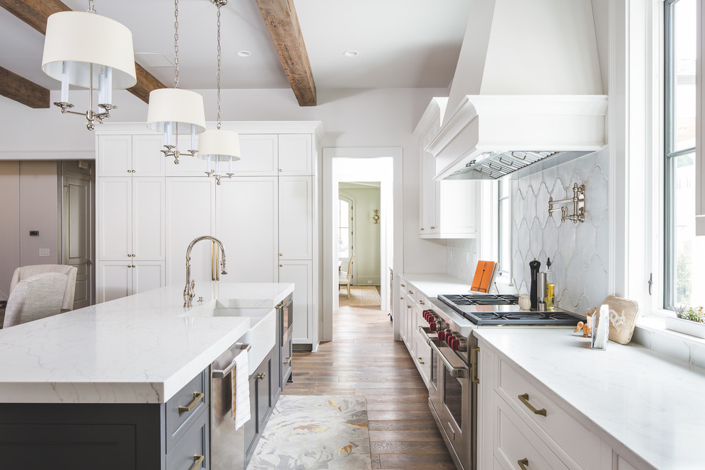 Traditional open plan kitchen in Atlanta with a farmhouse sink, beaded inset cabinets, white cabinets, quartzite benchtops, white splashback, ceramic splashback, stainless steel appliances, light hardwood floors, with island, brown floor and white benchtop.
