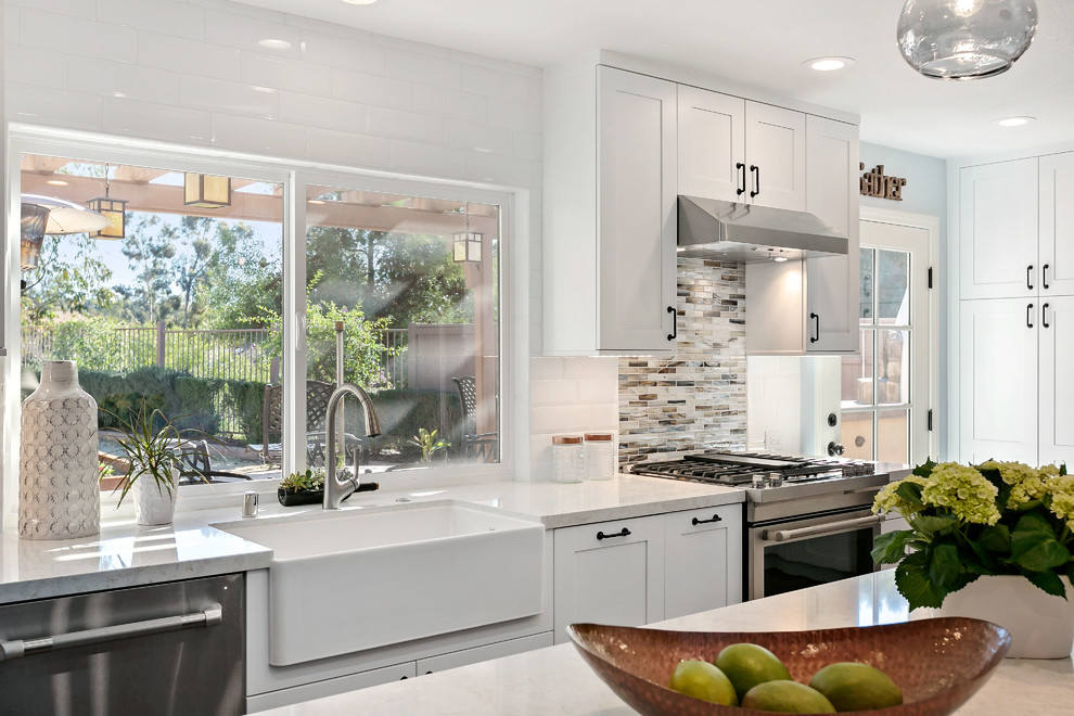 Design ideas for a large transitional l-shaped open plan kitchen in Tampa with a farmhouse sink, shaker cabinets, white cabinets, quartz benchtops, white splashback, porcelain splashback, stainless steel appliances, vinyl floors, with island, brown floor and white benchtop.