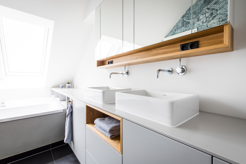 This is an example of a mid-sized scandinavian 3/4 bathroom in Munich with flat-panel cabinets, grey cabinets, a drop-in tub, white walls, cement tiles, a vessel sink, black floor and grey benchtops.