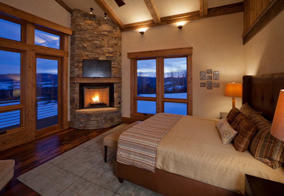 Inspiration for a country master bedroom in Denver with beige walls, medium hardwood floors, a corner fireplace and a stone fireplace surround.