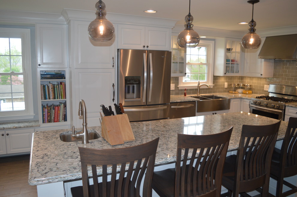 Example of a large transitional u-shaped ceramic tile and gray floor enclosed kitchen design with a farmhouse sink, raised-panel cabinets, white cabinets, quartz countertops, gray backsplash, glass tile backsplash, stainless steel appliances and an island