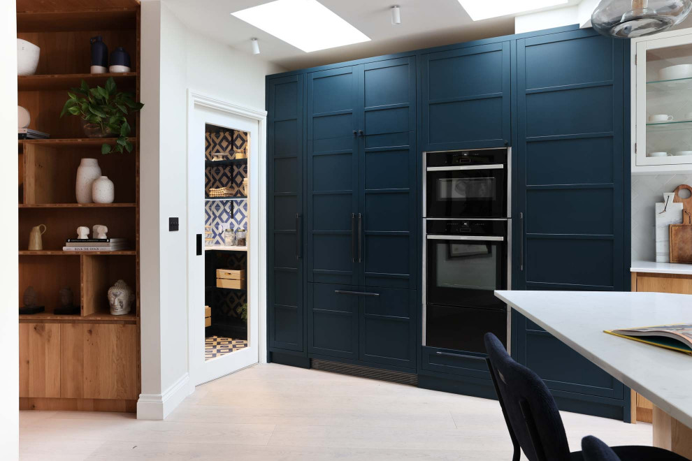 Inspiration for a large single-wall open plan kitchen in London with an integrated sink, shaker cabinets, blue cabinets, quartz worktops, white splashback, cement tile splashback, stainless steel appliances, light hardwood flooring, an island and white worktops.