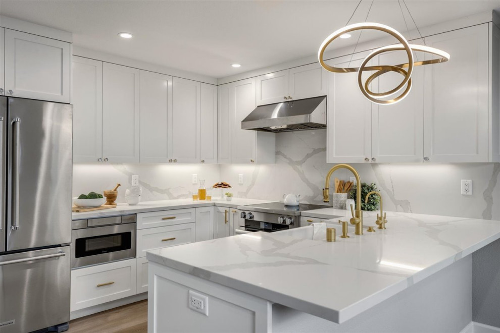 This is an example of a medium sized modern u-shaped kitchen/diner in San Francisco with a belfast sink, shaker cabinets, white cabinets, engineered stone countertops, white splashback, engineered quartz splashback, stainless steel appliances, vinyl flooring, a breakfast bar, beige floors and white worktops.