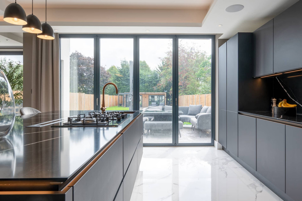 Design ideas for a large modern l-shaped open plan kitchen in Hertfordshire with flat-panel cabinets, black splashback, black appliances, marble flooring, an island, black worktops and a drop ceiling.