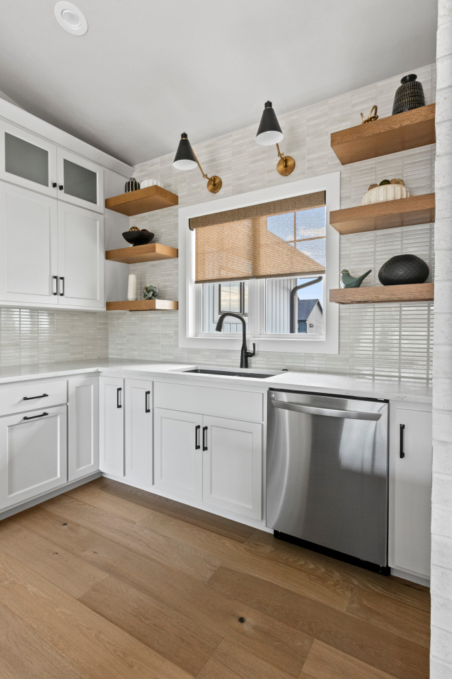 Inspiration for a mid-sized transitional l-shaped medium tone wood floor, brown floor and vaulted ceiling eat-in kitchen remodel with an undermount sink, shaker cabinets, white cabinets, quartz countertops, white backsplash, porcelain backsplash, stainless steel appliances, an island and white countertops