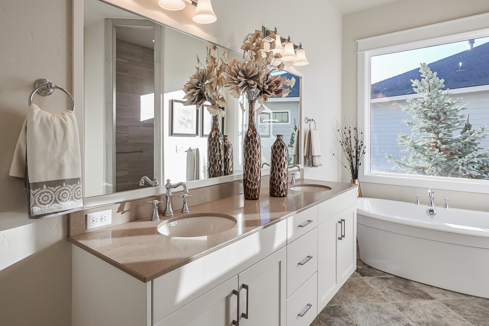 Transitional master bathroom in Boise with an undermount sink, shaker cabinets, white cabinets, quartzite benchtops, a freestanding tub, beige tile, porcelain tile, beige walls and limestone floors.