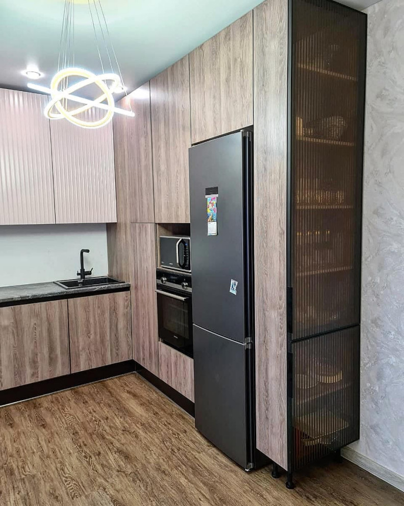Photo of a large transitional l-shaped eat-in kitchen in Moscow with a drop-in sink, louvered cabinets, grey cabinets, wood benchtops, white splashback, limestone splashback, black appliances, laminate floors, no island, brown floor and black benchtop.