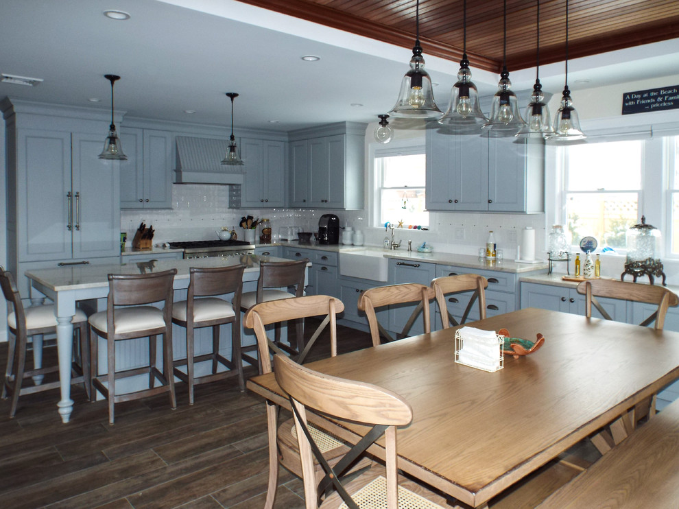 This is an example of a large beach style l-shaped eat-in kitchen in New York with with island, recessed-panel cabinets, grey cabinets, marble benchtops, white splashback, porcelain splashback, stainless steel appliances, a farmhouse sink and ceramic floors.