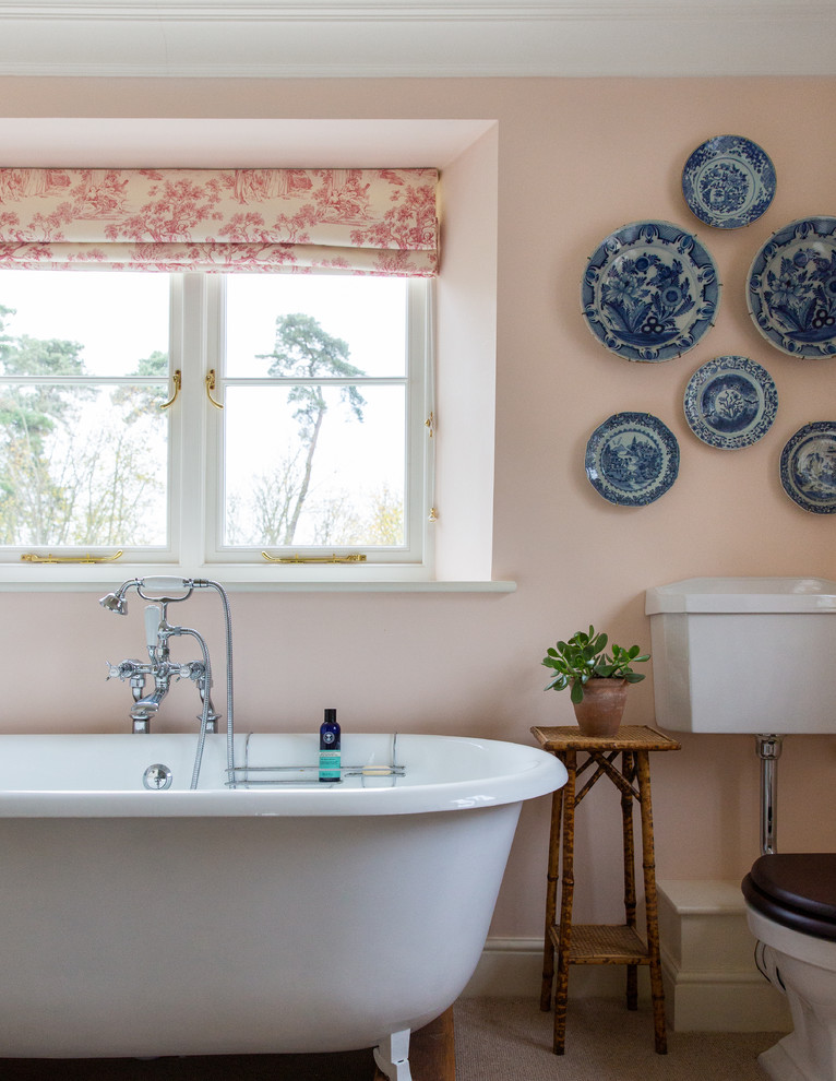 Traditional master bathroom in London with a claw-foot tub, a two-piece toilet, pink walls and beige floor.