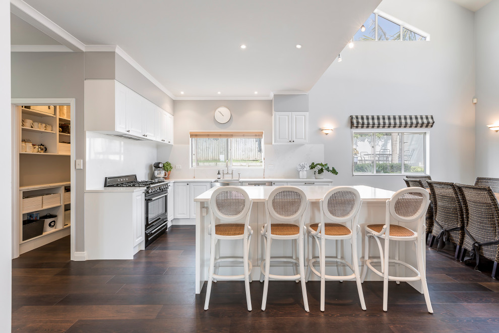 Design ideas for a mid-sized contemporary l-shaped eat-in kitchen in Auckland with a farmhouse sink, raised-panel cabinets, white cabinets, laminate benchtops, white splashback, dark hardwood floors, with island and white benchtop.