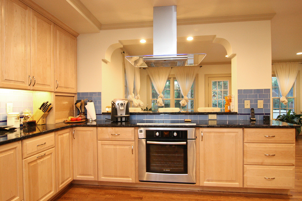 Huge transitional l-shaped medium tone wood floor open concept kitchen photo with an undermount sink, raised-panel cabinets, light wood cabinets, granite countertops, blue backsplash, glass tile backsplash and stainless steel appliances
