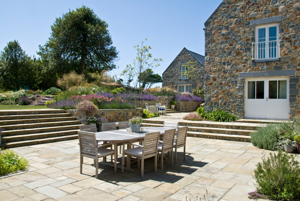 Inspiration for a large country backyard patio in Channel Islands with natural stone pavers.