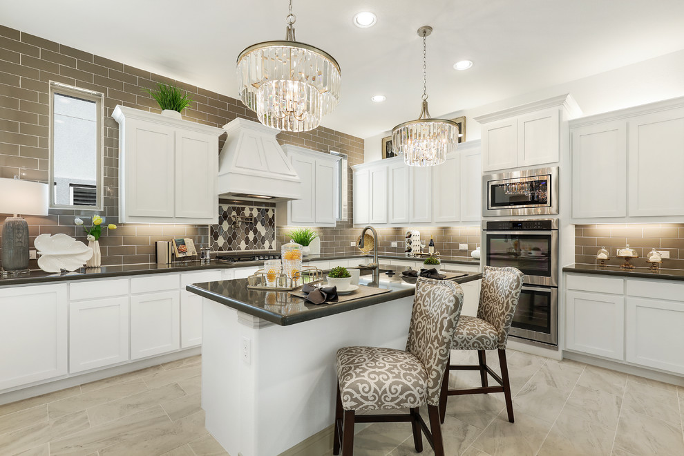 This is an example of a large traditional l-shaped kitchen in Dallas with white cabinets, granite benchtops, subway tile splashback, stainless steel appliances, ceramic floors, with island, shaker cabinets, grey splashback, grey floor and black benchtop.