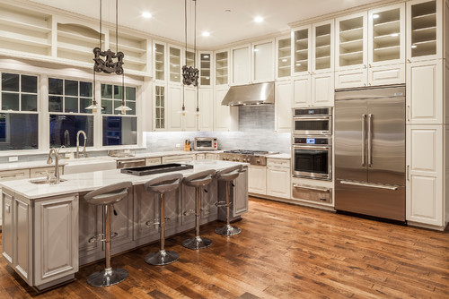 Bright open concept kitchen with large island, bar stools and white shaker kitchen cabinets surrounding stainless steel appliances
