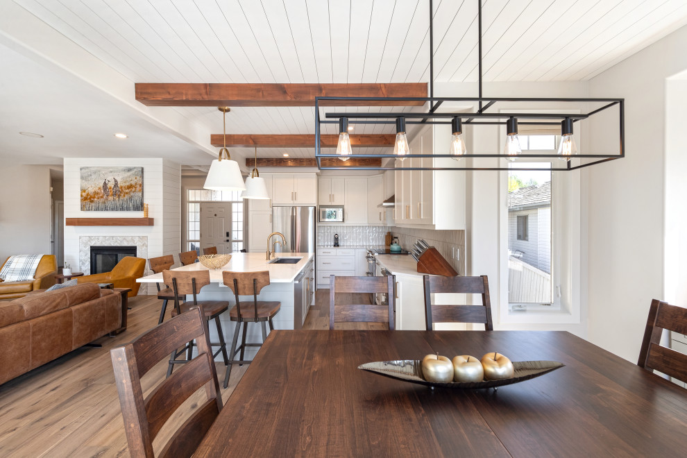 This is an example of a mid-sized country open plan dining in Edmonton with white walls, vinyl floors, a two-sided fireplace, brown floor and timber.