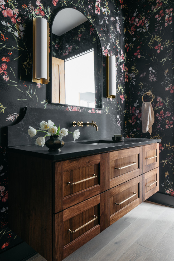 Exemple d'un WC et toilettes chic en bois foncé avec un placard à porte shaker, un mur multicolore, parquet clair, un lavabo encastré, un sol gris, un plan de toilette noir, meuble-lavabo suspendu et du papier peint.