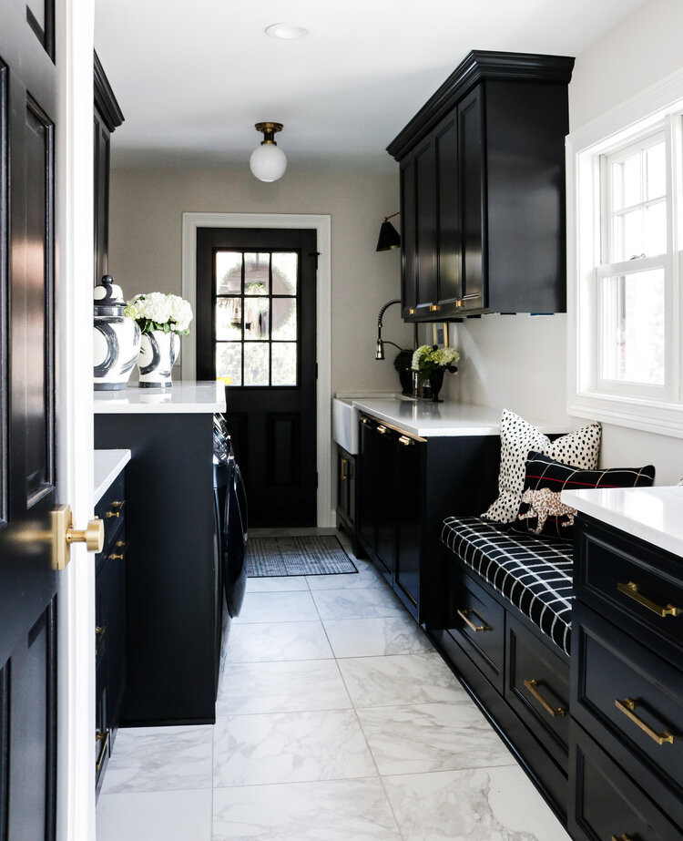This is an example of a traditional galley utility room in Milwaukee with a farmhouse sink, black cabinets, quartzite benchtops, white walls, ceramic floors, a side-by-side washer and dryer, white floor and white benchtop.