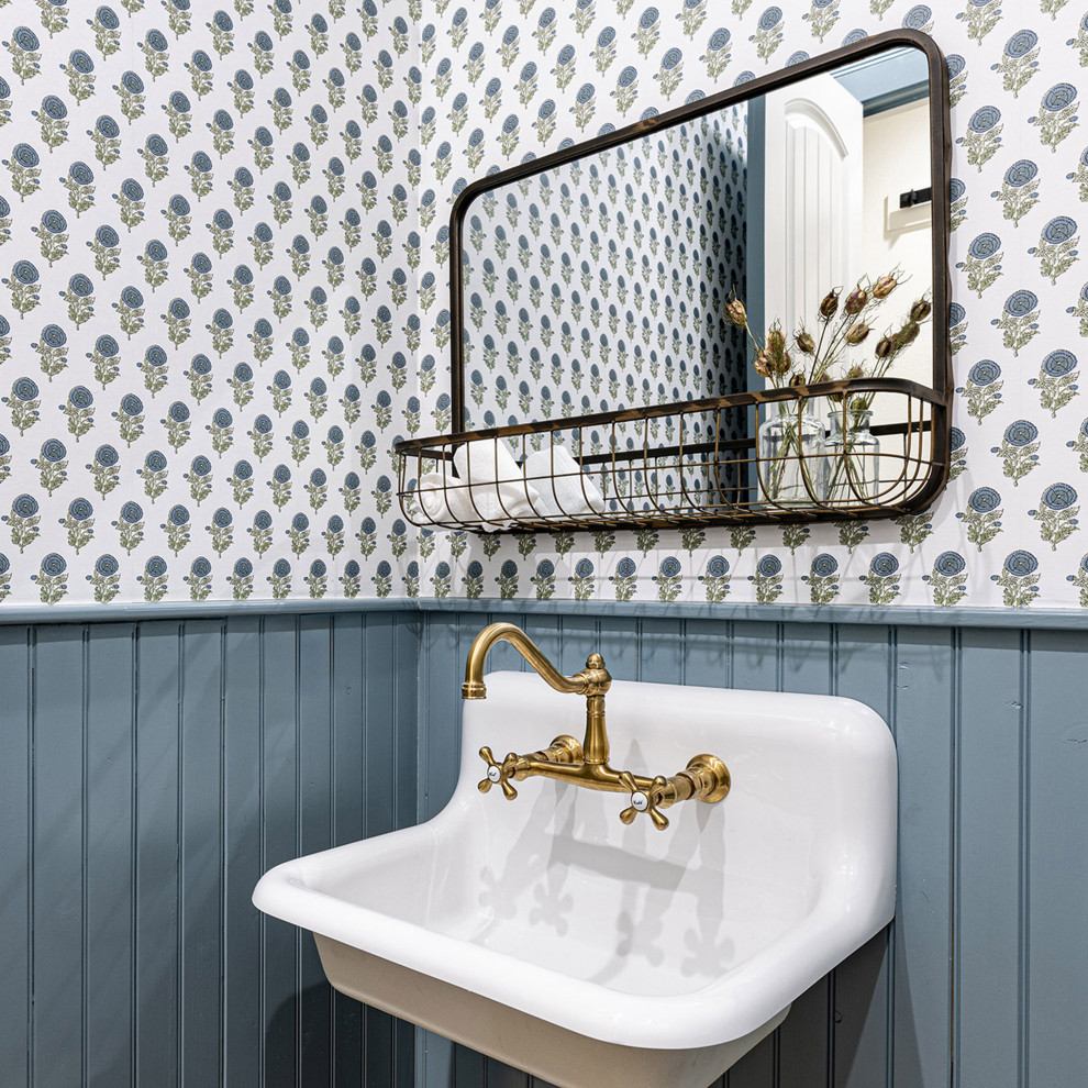 Small country powder room in Dallas with a one-piece toilet, blue walls, brick floors, a wall-mount sink, brown floor, wallpaper and decorative wall panelling.